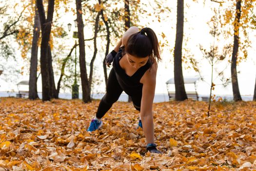 Attractive woman in sports clothes doing sports exercises in nature, on the carpet of autumn leaves, loves gymnastics, kneads his legs. Active young girl engaged in sports, leads a healthy lifestyle.