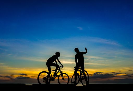 Two Cyclists with their bicycles at the beach, sunset scene.