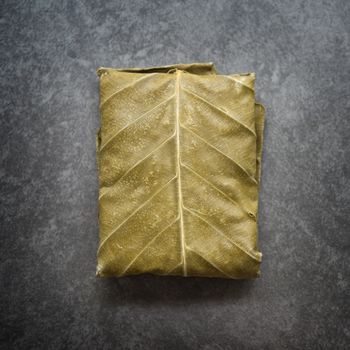 Fresh raw tempeh wrapped in leaf on dark background, vegetarian food. Top view.