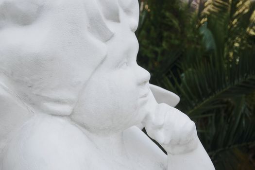 White statue of the angel against the background of palm trees