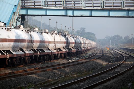 A train carrying fuel stationed around a curve at a railway station in India, in morning.