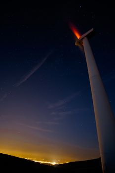 Long time exposure of wind turbine at night with an almost clear sky and the city lights