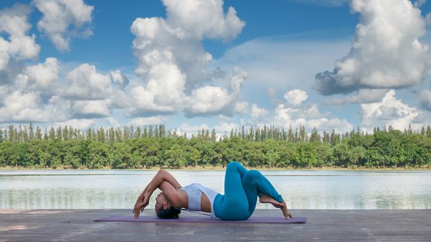 Asian woman practicing yoga pose , exercise outdoors with view of beautiful lake - relax in nature