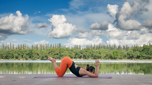 Asian woman practicing yoga pose , exercise outdoors with view of beautiful lake - relax in nature