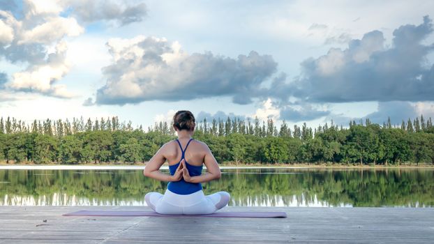 Asian woman practicing yoga pose , exercise outdoors with view of beautiful lake - relax in nature