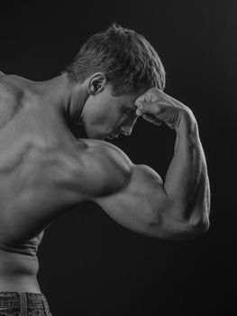 Muscular athlete flexing his arm demonstrating biceps with his back to the camera