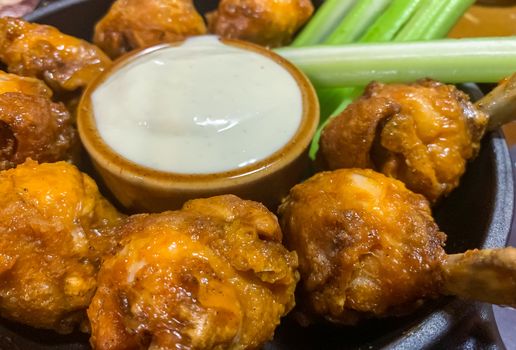 Delicoius chicken wings and celery sticks placed in a round plate with a small bow of white sause in the middle