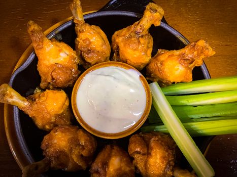 Delicoius chicken wings and celery sticks placed in a round plate with a small bow of white sause in the middle