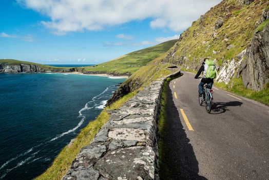 A cyclist riding his bike in the early morning. The road is in the middle of the mountains and the coast in Ireland.