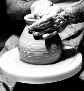A close view of the hands of a craftsman while modeling the clay pot over the rolling table.