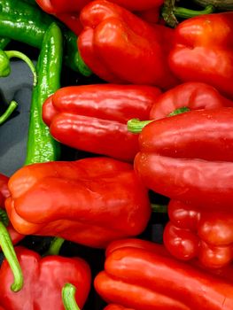 A close-up of fresh peppers. Most of them are red contrasting with the few green ones. Great vivid colours.