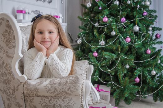 Cute smiling little girl near christmas tree sitting armchair