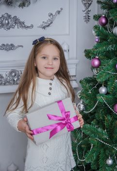 Cute smiling little girl with gift box near Christmas tree