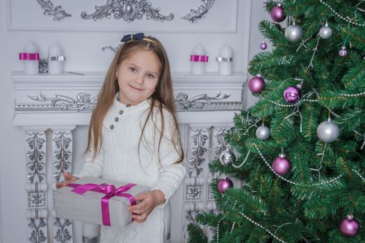Cute smiling little girl iwith gift box near Christmas tree