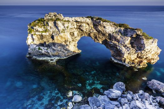 A rocky arch in the clear, blue sea water of Mallorca