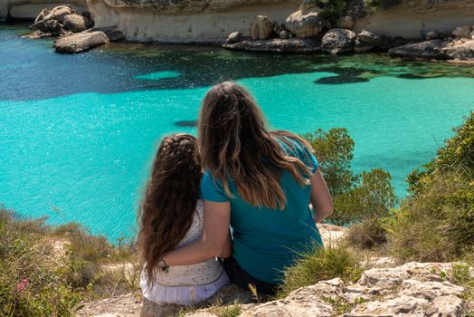 Mother and daughter enjoying the beautiful view of the turquoise water of the Mediterranean sea in Mallorca