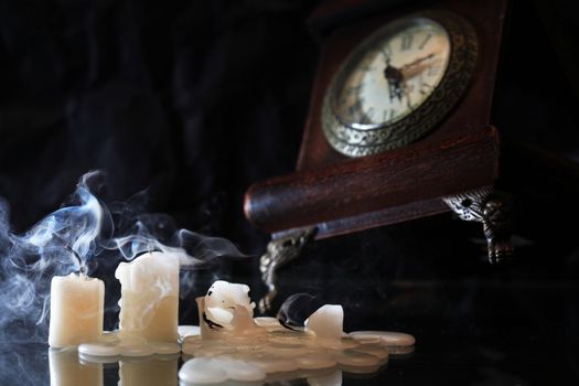 Set of extinguished candles near old clock on nice dark background