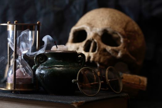 Ancient science concept. Human skull on old book near hourglass and candle