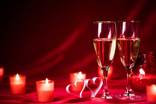 Valentines day celebration, glasses of champagne, candles, roses and hearts on red silk