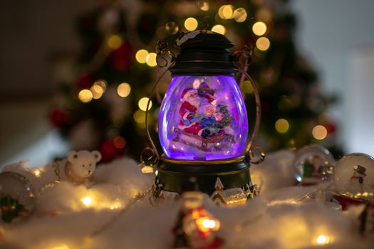 Christmas decoration, snow dome, globe with table decoration, Santaclaus on sleigh with child in winter scene, christmas tree with lights in background, selective focus