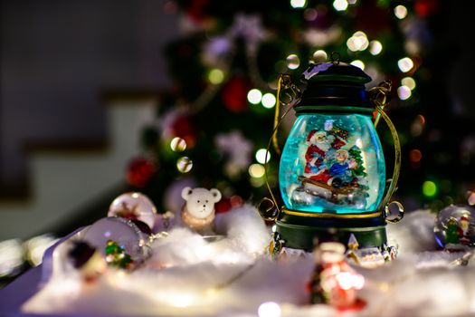 Christmas decoration, snow dome, globe with table decoration, Santaclaus on sleigh with child in winter scene, christmas tree with lights in background, selective focus