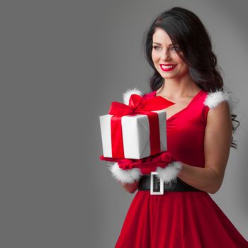 Happy woman in red santa claus outfit holding Christmas present