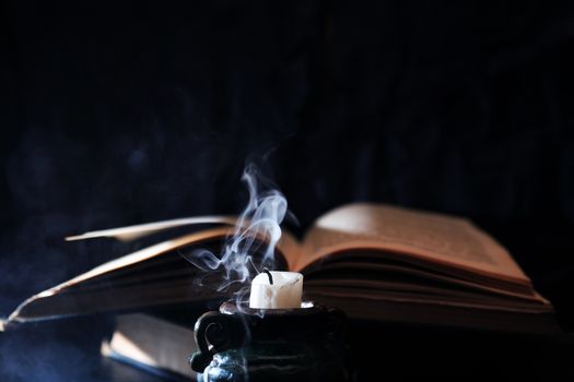 Still life with extinguished candle and blue smoke near old book