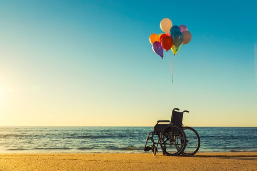 Wellchair on a beach with colored  ballons 