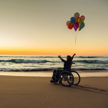 Handicapped woman on a wheelchair with colored balloons at the beach