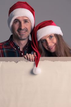 Happy couple in Santa hats holding blank banner with copy space