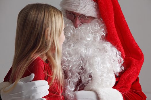 Little girl sitting on santa claus knees and talking to him