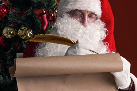 Santa Claus sitting at home and writing on old paper roll to do list with quill pen and ink