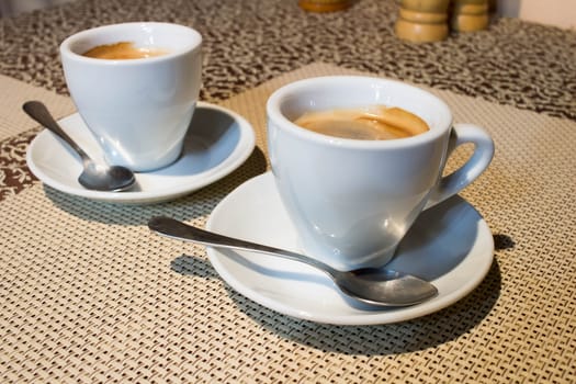 Composition of two cups of coffee on white serving plates with small metal spoons