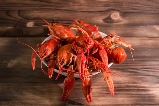 Plate of red boiled crayfishes with claws on wooden background