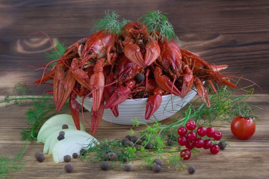 Plate of red boiled crayfishes with claws and fennel, onions, tomato and peppers on wooden background