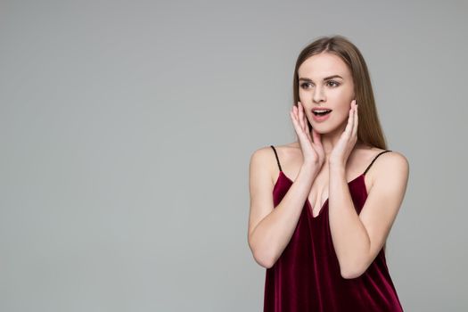 Portrait of posing young model long-haired blond girl in dark red dress showing emotions