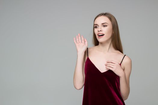Portrait of posing young model long-haired blond girl in dark red dress showing emotions