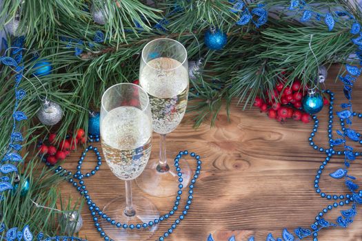 Christmas and New Year still life composition with two champaign glasses, pine tree acerose, red rowan berries, blue and silver balls, garland ornament decoration, copy space