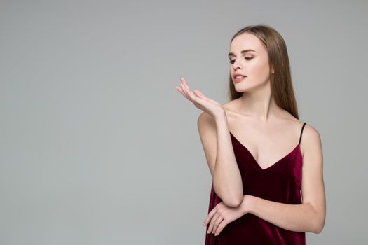 Portrait of posing young model long-haired blond girl in dark red dress showing emotions: desire to something in her hand