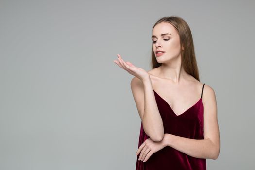 Portrait of posing young model long-haired blond girl in dark red dress showing emotions: desire to something in her hand