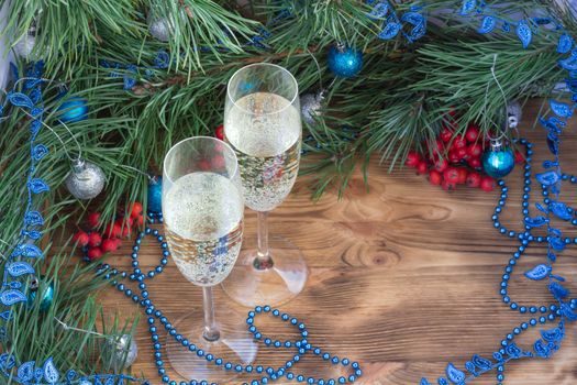 Christmas and New Year still life composition with two champaign glasses, pine tree acerose, red rowan berries, blue and silver balls, garland ornament decoration, copy space