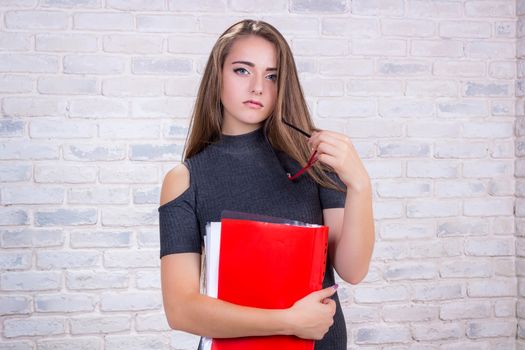 Young beautiful girl model with long hair imitates business lady, office manager or administrator with red folder of documents
