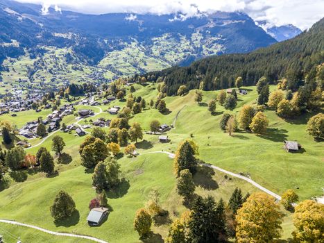 Amazing dream like Swiss alpine mountain landscape, wooden chalets on green fields and high mountains with snowy peaks background, in Grindelwald of Switzerland.