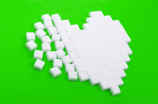 Broken heart made of sugar cubes lies on a green background