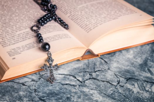 Black rosary and cross on the Bible on a gray table. Religion at school.