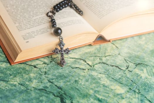 Black rosary and cross on the Bible on a green surface. Religion at school.