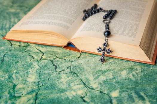 Black rosary and cross on the Bible on a green surface. Religion at school.