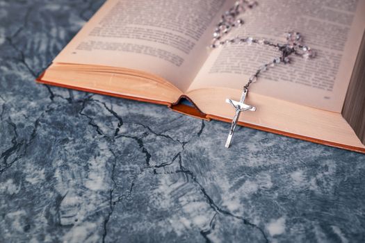 Silver rosary and cross with jesus on the Bible on a gray table. Religion at school.