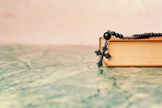 Black rosary and cross on the Bible on a green table. Religion at school,vintage style.