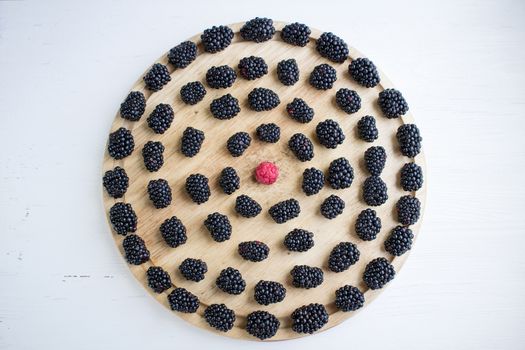 Tasty juicy berries set of many blackberries and one raspberry among them on round wooden tray